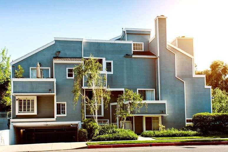 3-story apartment building with painted blue siding and white trim, balcony patios, fireplaces, and gated subterranean parking.